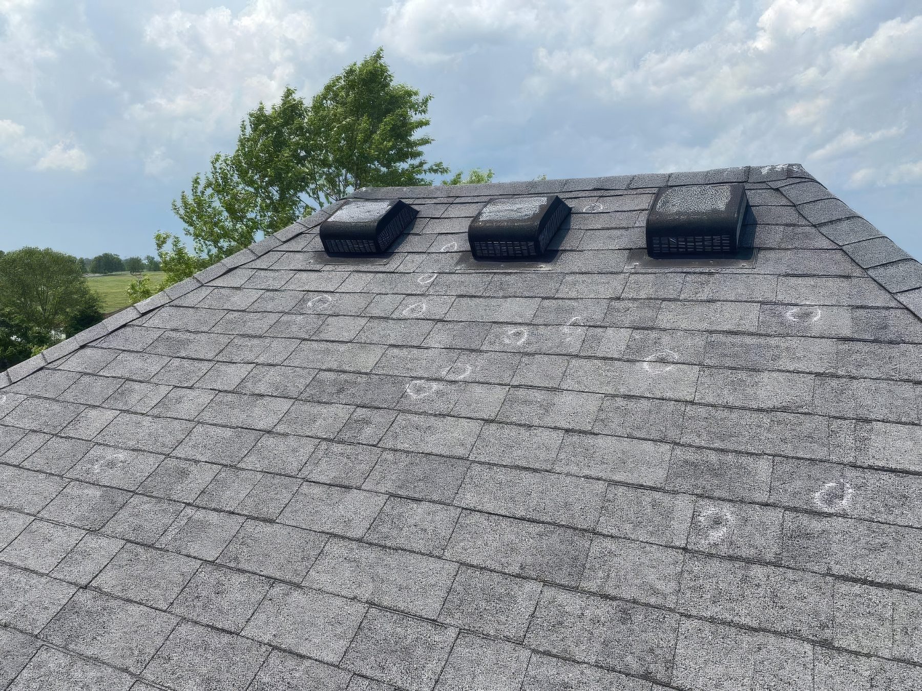 A roof after a hailstorm, the hits circled in chalk around three box vents, under a clearing sky
